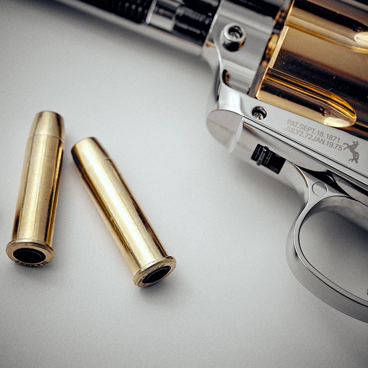 Colt SAA 'Smoke Wagon' CO2 Pistol 5 A close-up of a silver Colt SAA CO2 Smoke Wagon Pistol .177 Pellet with a gold cylinder and two brass .177 pellet bullets on a white surface.
