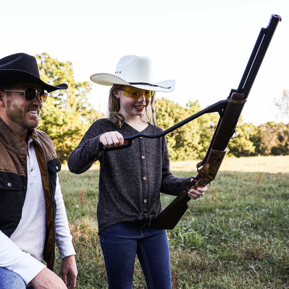 Barra 1866 Junior Lever Action Pneumatic Air Rifle Kit 3 A man and a young girl wearing cowboy hats and safety glasses stand outdoors, while the girl holds and loads a Barra 1866 Junior Pneumatic Air Rifle Kit.